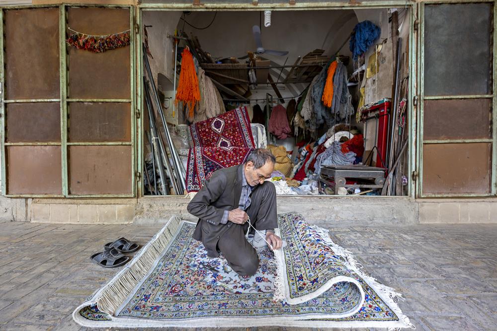 Man arranges the fringes of Persian carpet in the bazaar in Yazd, Iran
