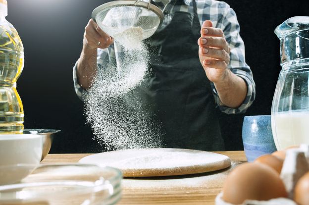 Image of professional male cook sprinkling flour on surfaces.