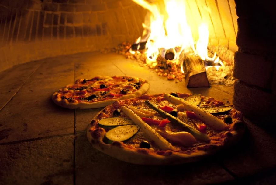 Picture of a pizza oven with burning wood, baking two delicious and palatable pizzas.