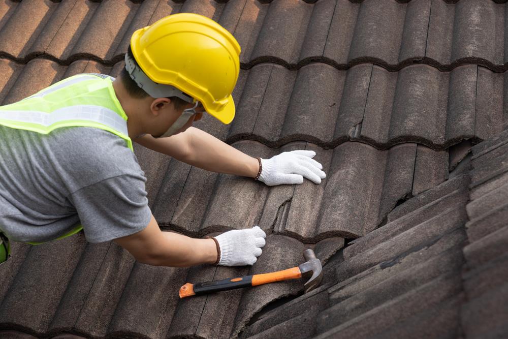 A worker replacing an old tile on a roof