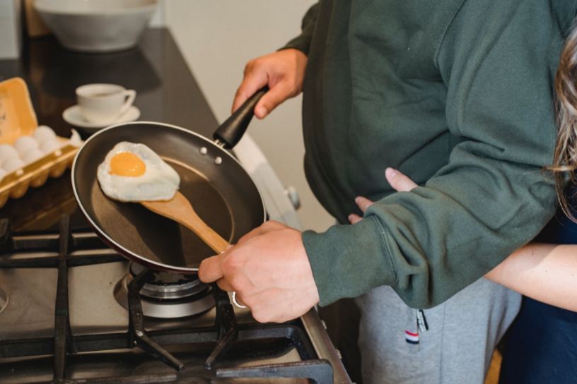 man-preparing-fried-egg-in-pan-in-kitchen-at-home