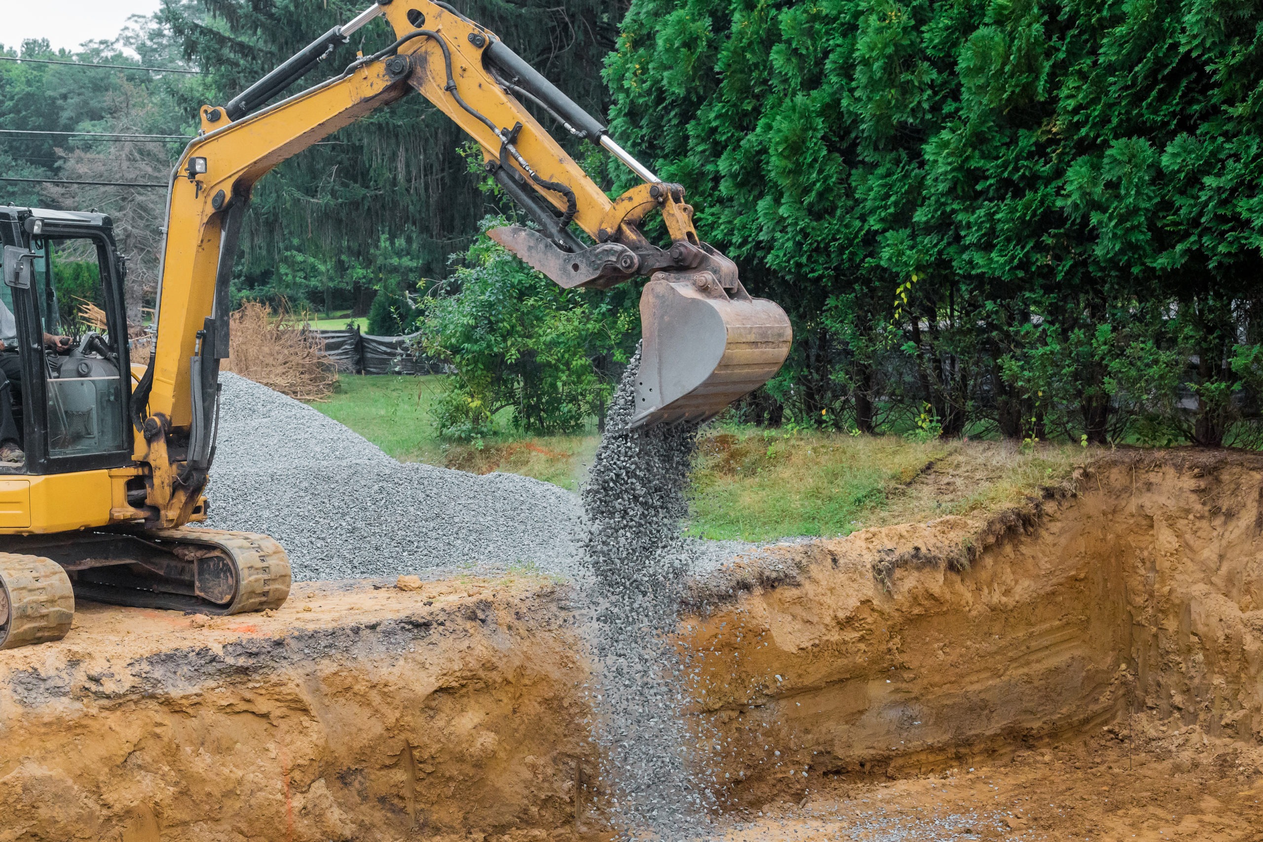 A yellow excavator bucket shovel moving stones gravel of foundation on a construction site