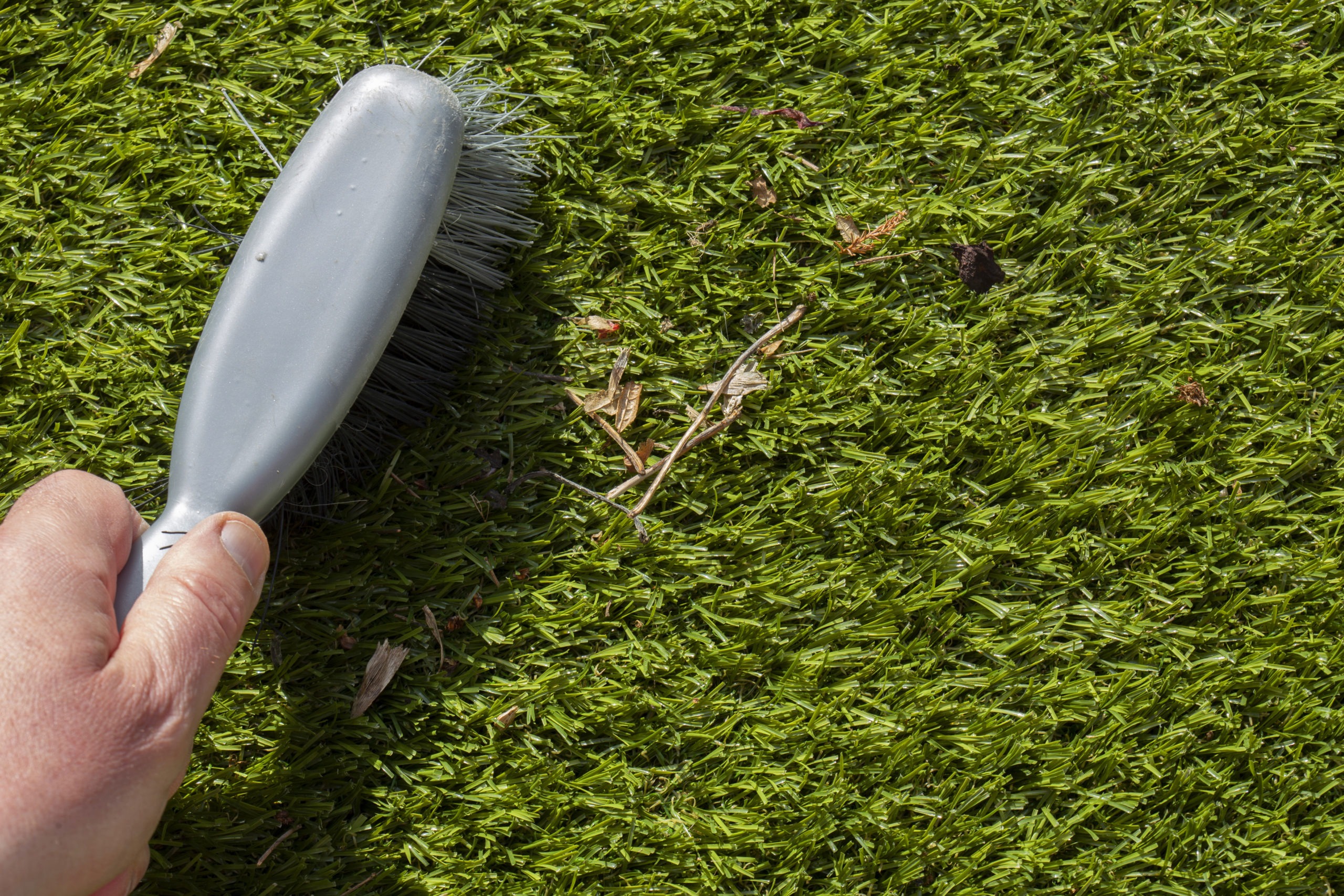 Man brushing rubbish on artifiicial grass turf with a hand brush