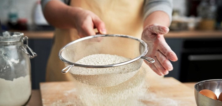 A person sifting flour in a domestic kitchen