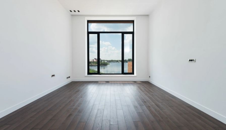 a spacious room with white walls, panoramic windows, wooden floors, and baseboards