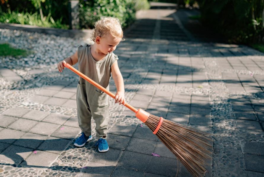 charming-child-sweeping-concrete-pavement-with-broomstick