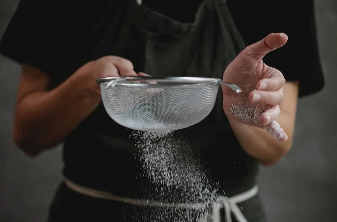 a person sifting flour using a strainer