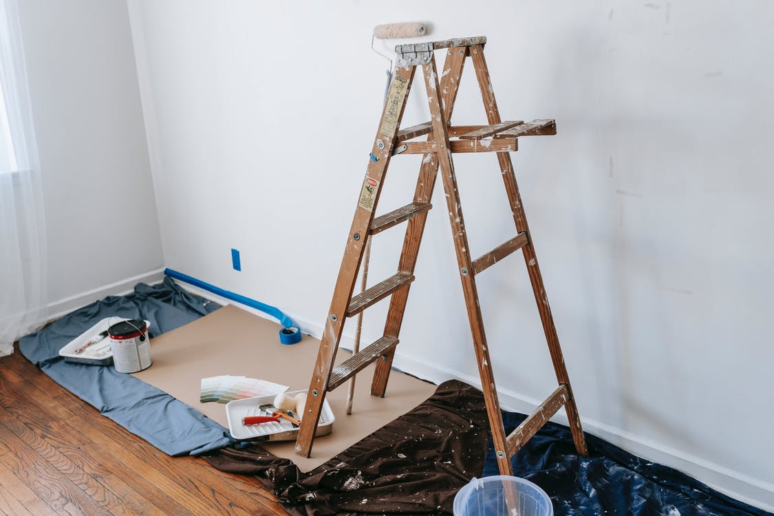 a dirty wooden stepladder and painting materials on drop sheets in a room