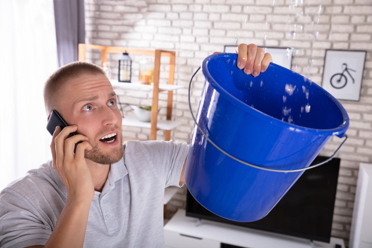  a man collecting water leakage in a bucket while calling the plumber