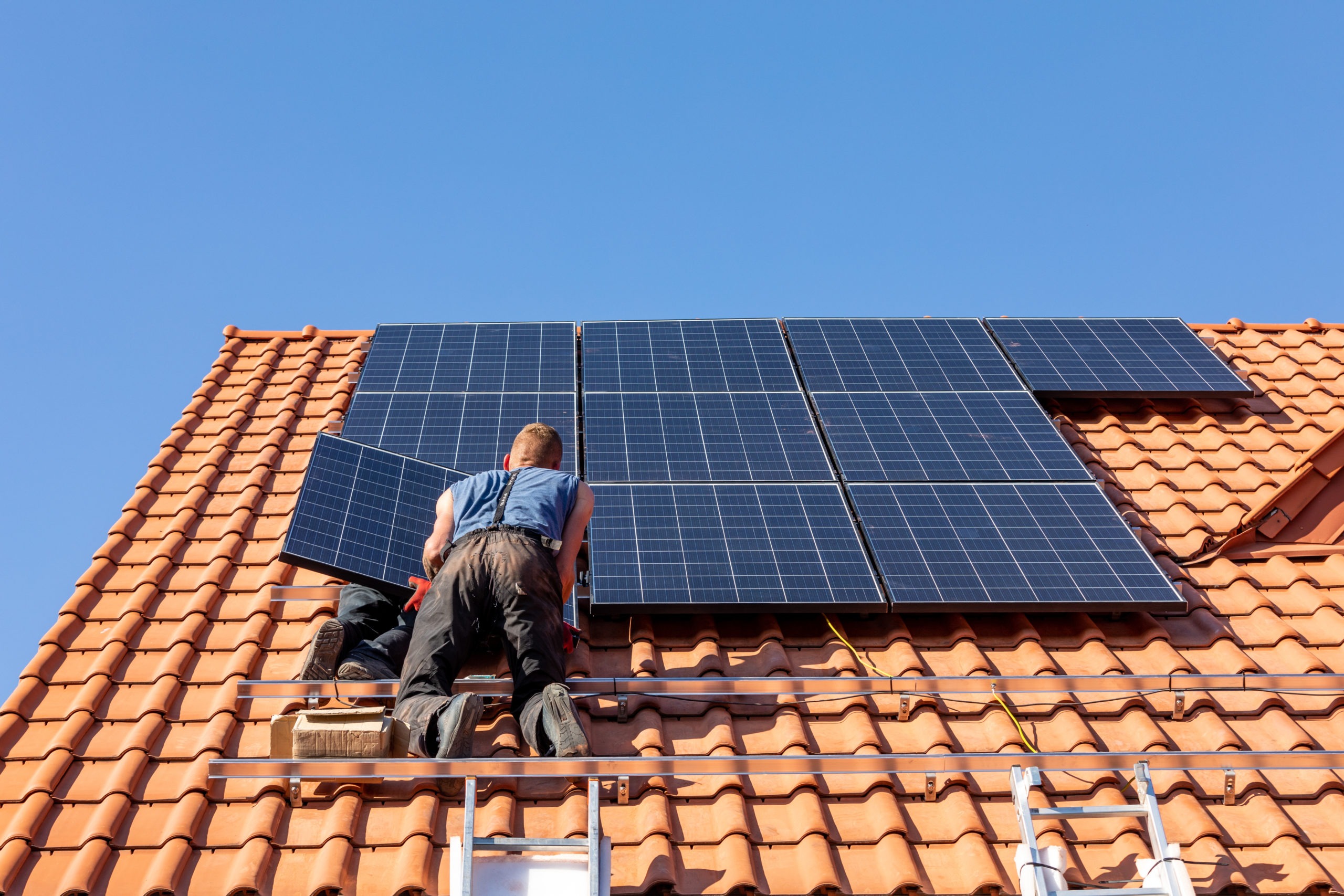 Workers installing solar electric panels on a house roof i