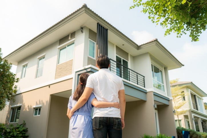 Back portrait of Asian young couple standing and hugging together looking happy in front of their new house to start new life. Family, age, home, real estate and people concept.