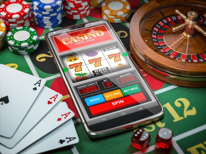 Casino online. Smartphone or mobile phone, slot machine, dice, cards and roulette on a green table in casino.