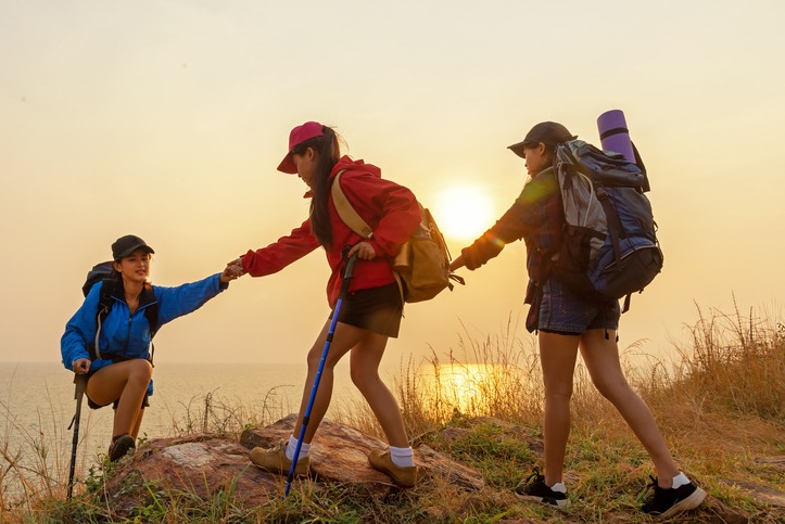 Group Hiker team woman helping her friend climb up the last section of sunset in mountains. Traveler teamwork and family relax walking in outdoor lifestyle adventure and camping. Travel summer life Concept.