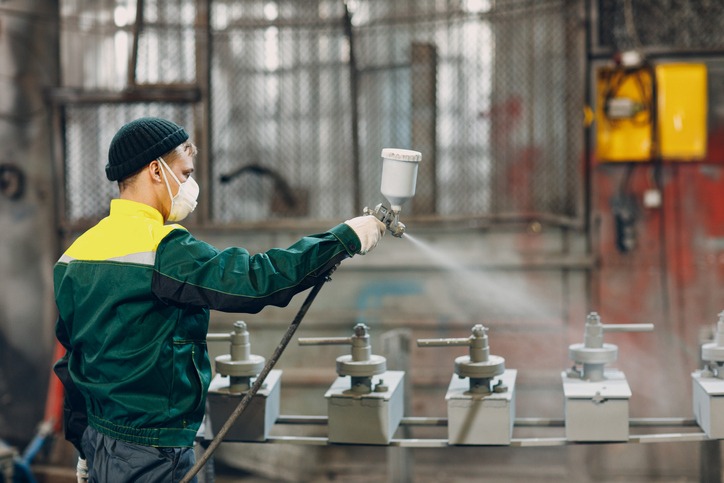 Powder primer coating of metal parts. Worker man in a protective suit sprays powder paint from gun on metal product construction at factory plant