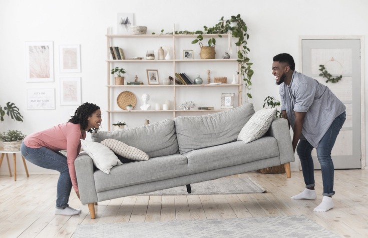 Black couple moving sofa in living room, replacing furniture at home