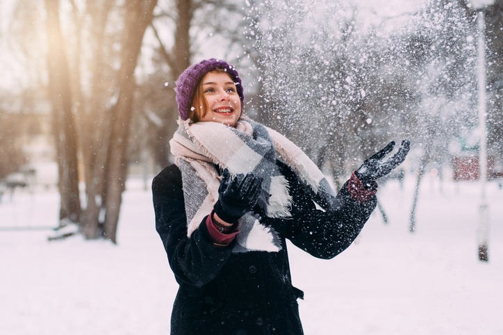 Portrait of young beautiful girl in winter. Smiling and enjoying snowfall on warm sunset. Snowy day