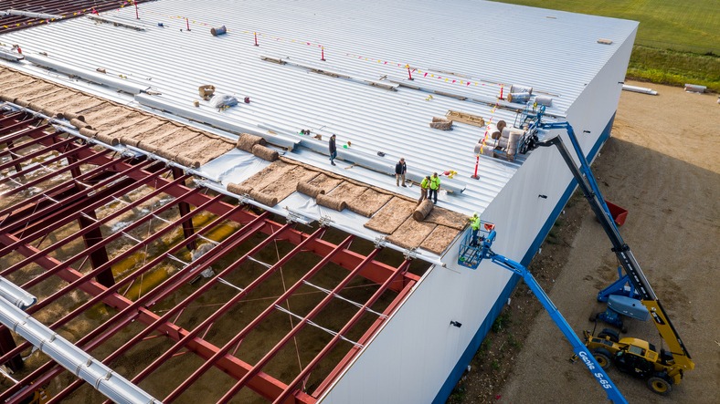 Construction workers installing roof panels on a warehouse.