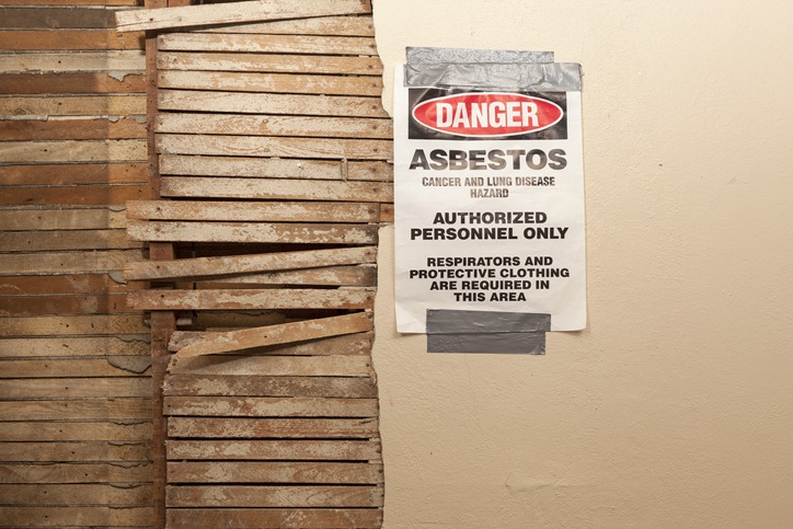 A Danger Asbestos Warning Sign Hangs Next to Exposed Broken Wood Wall