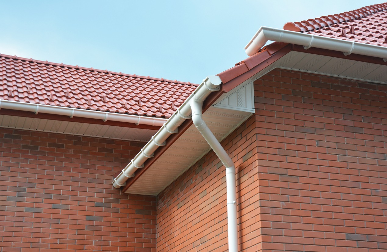 A close-up on plastic rain gutters, downspout, soffit, and fascia with a box-end on the corner of a brick house