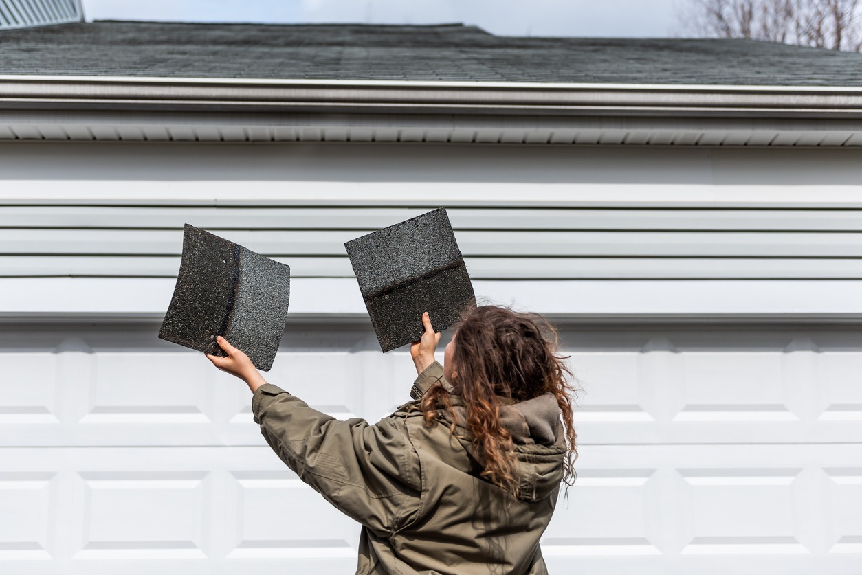 female homeowner standing in front of house garage holding two roof tile shingles