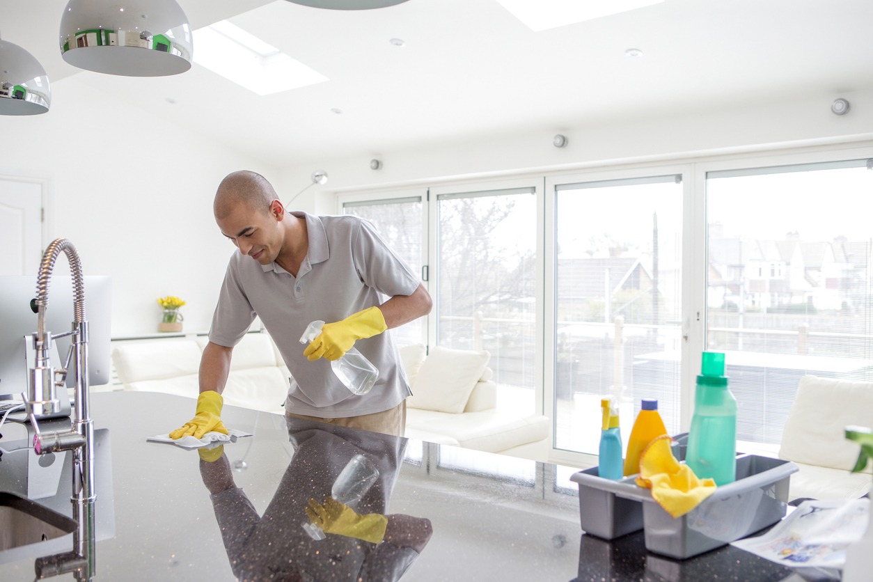 a man cleaning a kitchen countertop, with cleaning supplies and materials