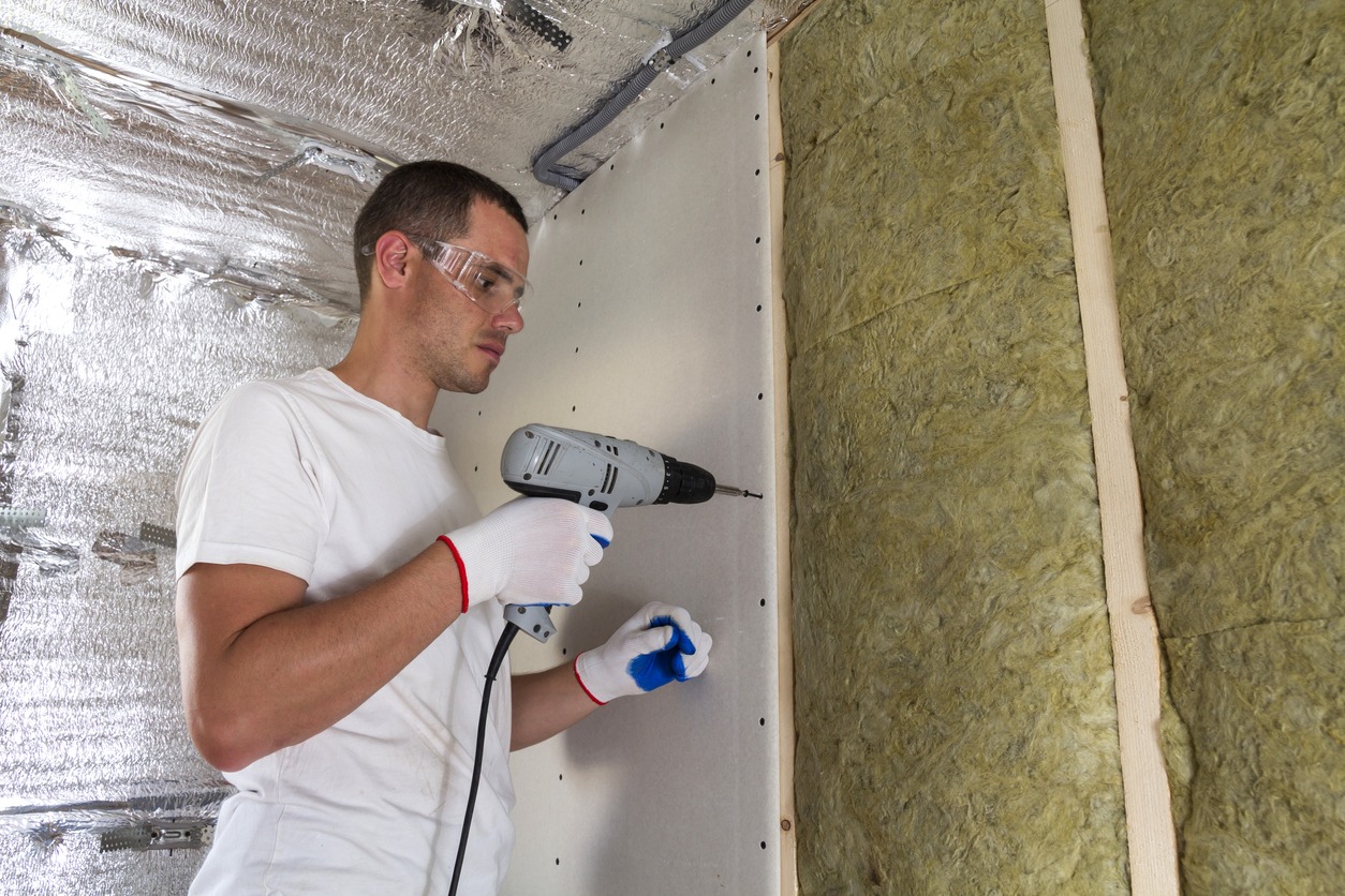 A Worker in goggles with screwdriver working on insulation garage walls