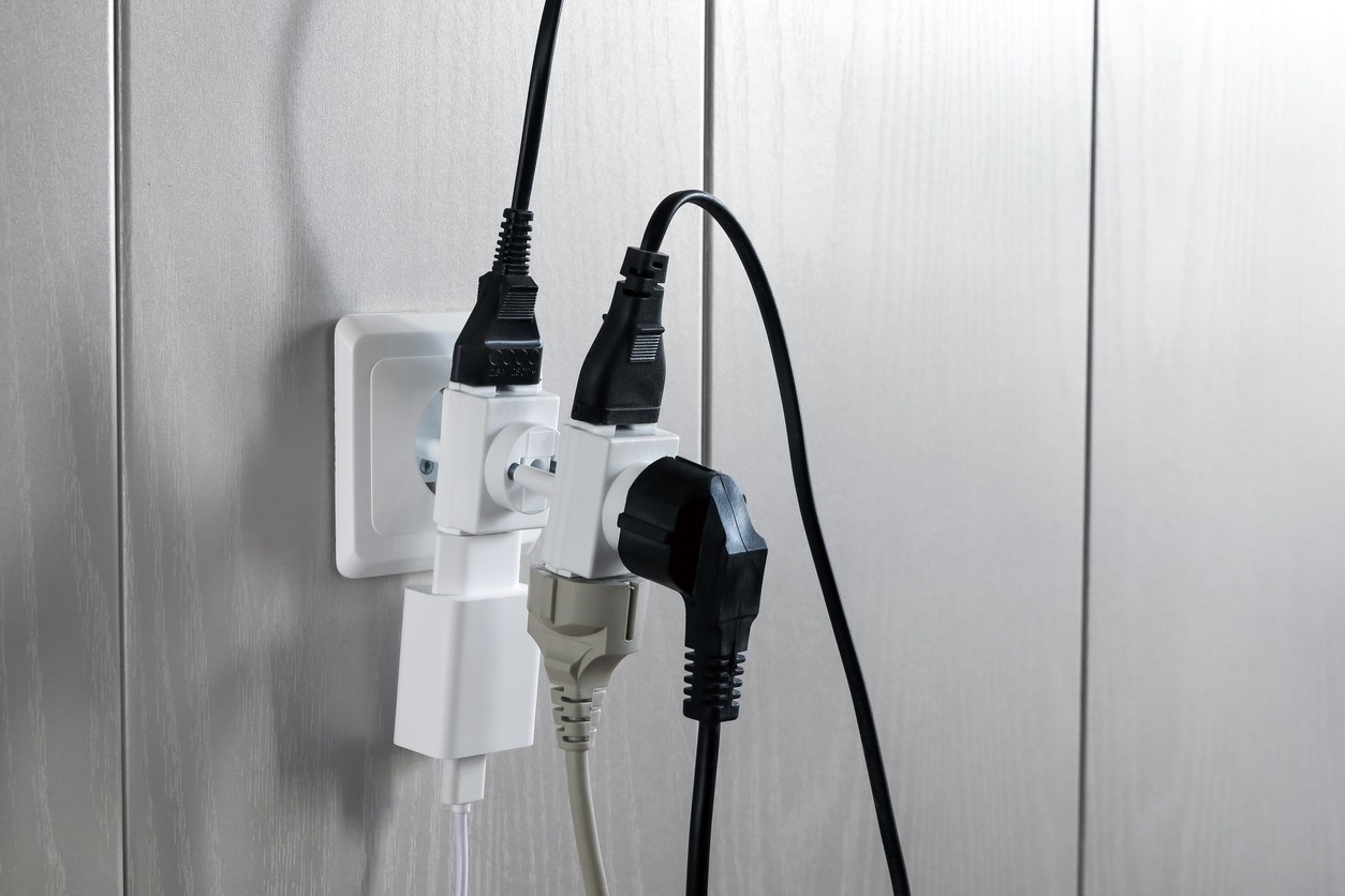 Multiple plugs in wall electrical outlet is dangerous overload, close-up with copy space