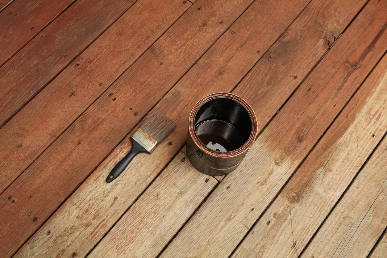 Partially stained deck; paint brush and a can of stain