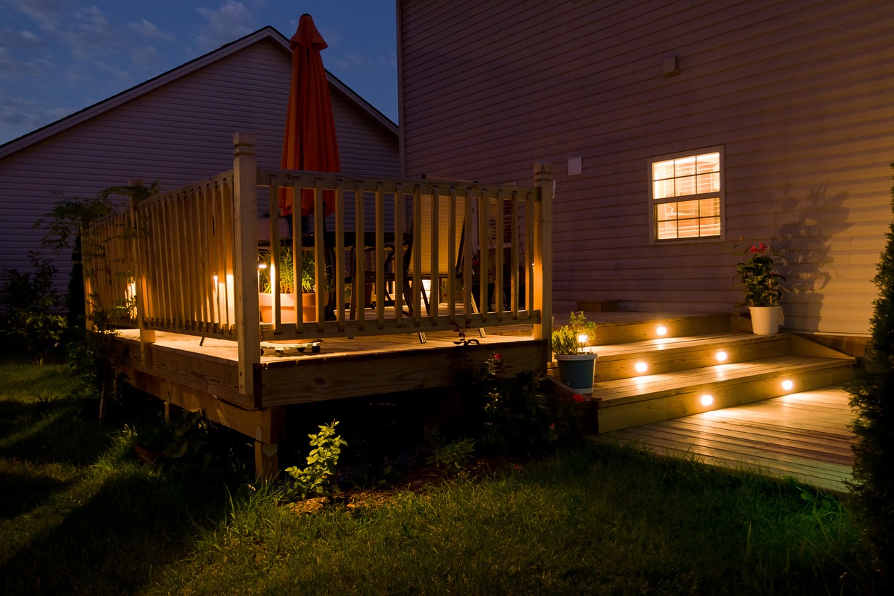 Wooden deck and patio of family home at night with stair lighting