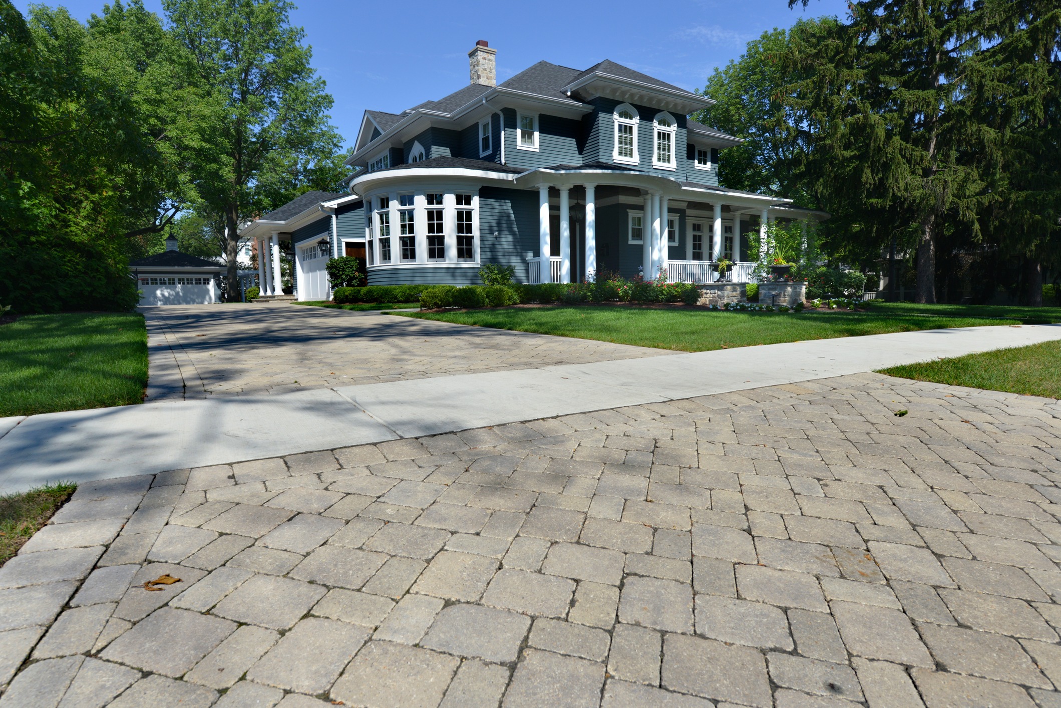 Large blue house on a lot with a long pavers driveway